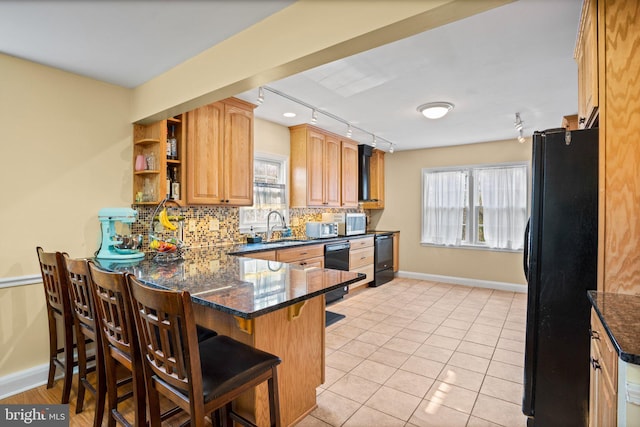 kitchen with a breakfast bar, black refrigerator, backsplash, dark stone countertops, and kitchen peninsula