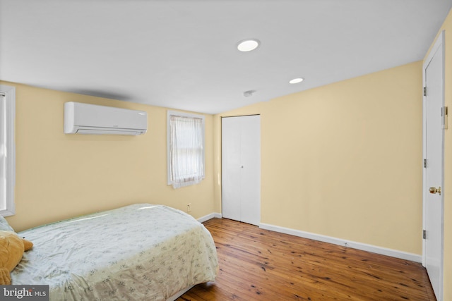 bedroom with hardwood / wood-style flooring, vaulted ceiling, a wall unit AC, and a closet