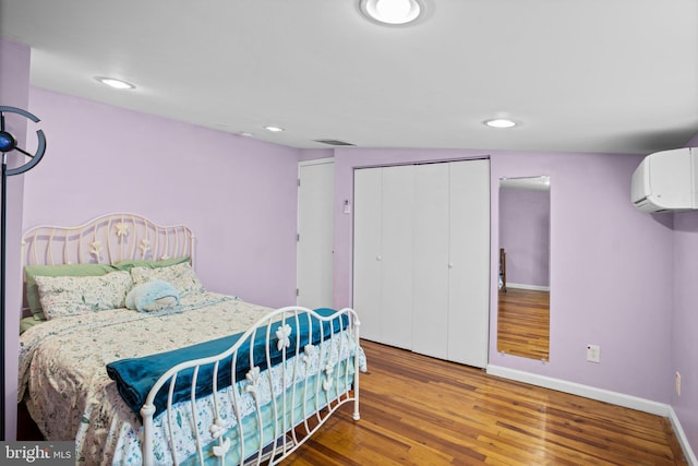 bedroom with hardwood / wood-style floors, a closet, and an AC wall unit