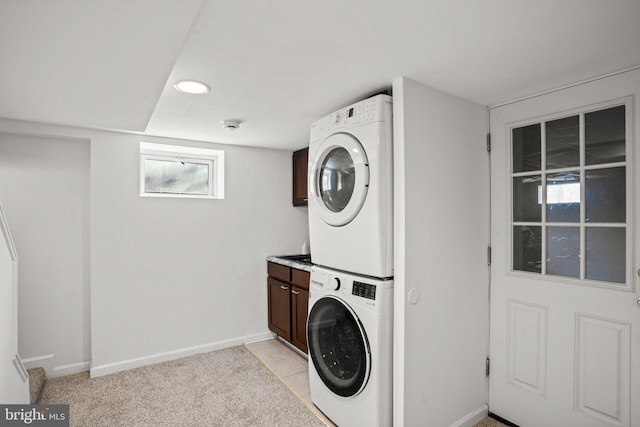 washroom featuring stacked washer and dryer, light colored carpet, and cabinets