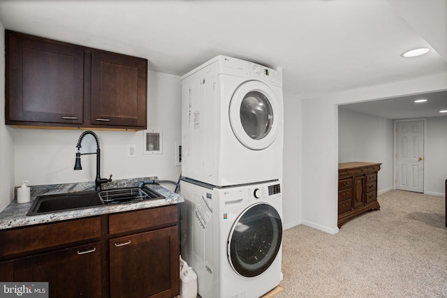 laundry area featuring cabinets, stacked washer / drying machine, sink, and light colored carpet