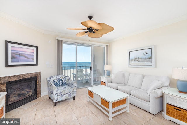 tiled living room with a fireplace, ornamental molding, ceiling fan, and a water view