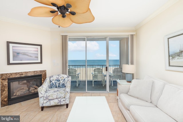 tiled living room with a fireplace, ornamental molding, ceiling fan, and a water view