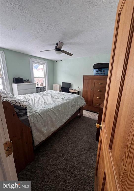 carpeted bedroom with ceiling fan, radiator, and a textured ceiling