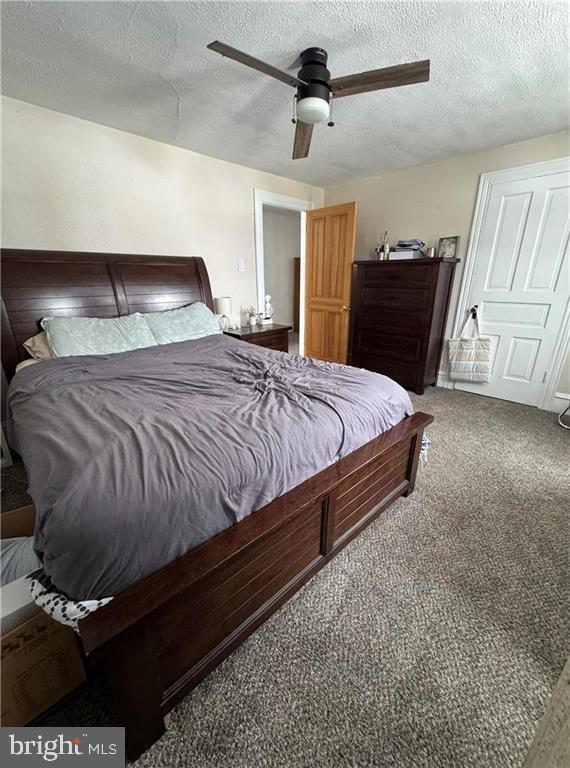 carpeted bedroom featuring ceiling fan and a textured ceiling