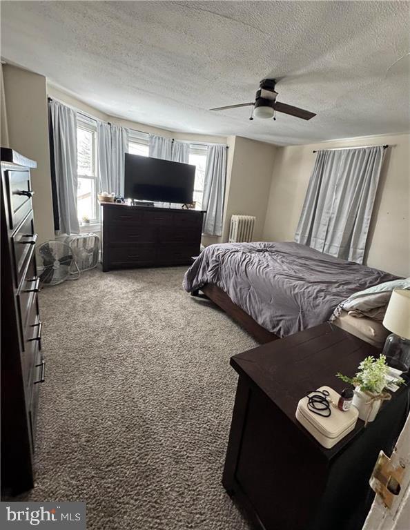 carpeted bedroom featuring ceiling fan, radiator heating unit, and a textured ceiling