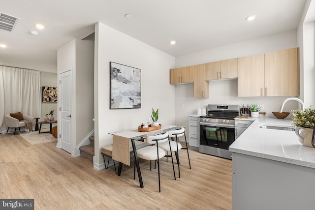 kitchen with electric stove, light stone countertops, sink, and light wood-type flooring