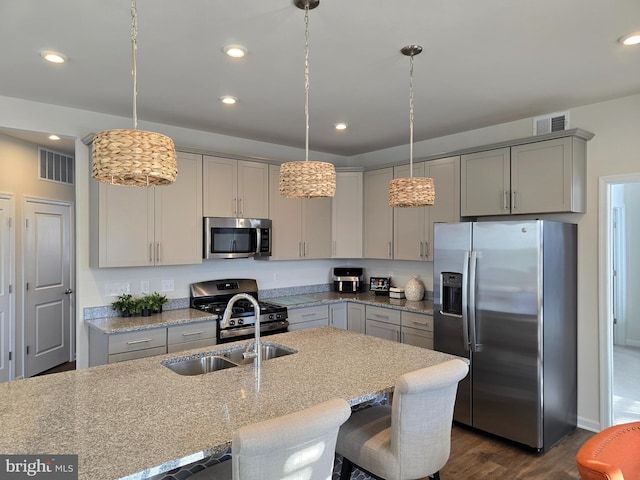 kitchen featuring sink, a breakfast bar area, stainless steel appliances, light stone countertops, and decorative light fixtures