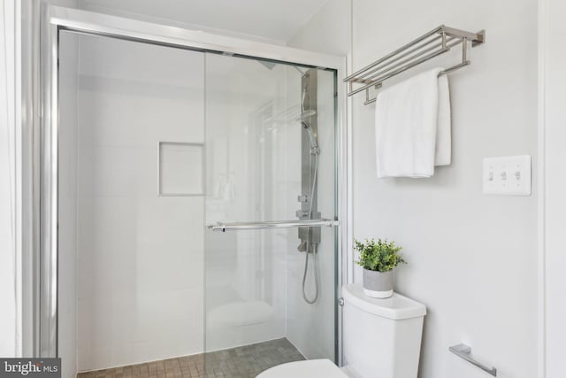 bathroom featuring a shower with door and toilet