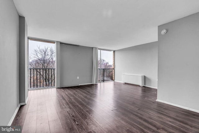 empty room with floor to ceiling windows, dark hardwood / wood-style floors, and radiator heating unit