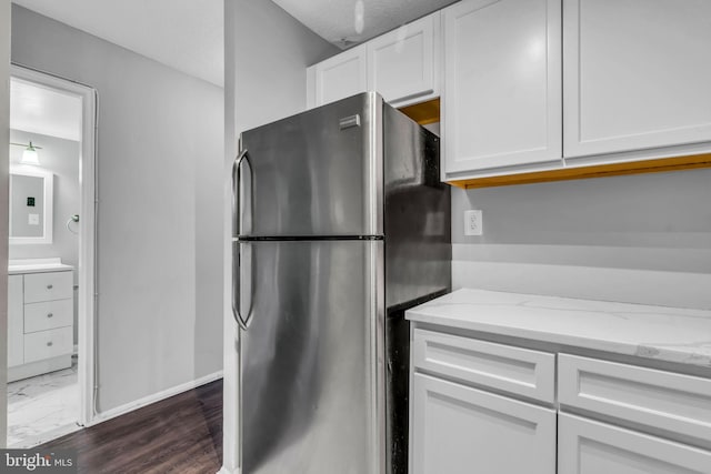 kitchen with stainless steel fridge, light stone countertops, and white cabinets