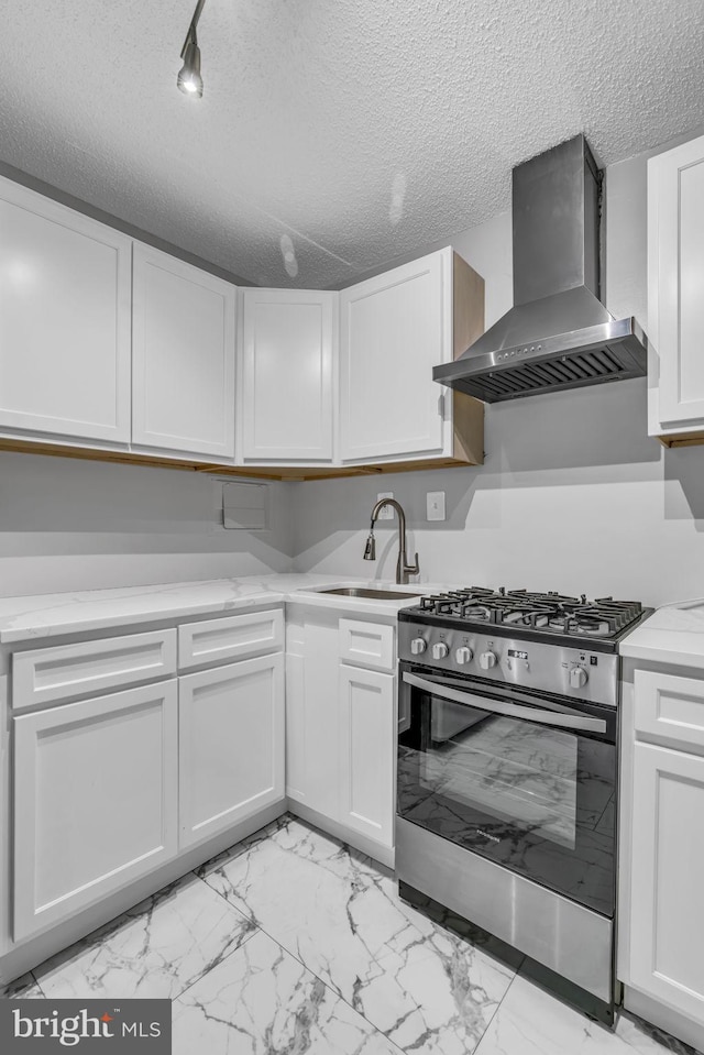 kitchen featuring sink, a textured ceiling, stainless steel range with gas cooktop, wall chimney range hood, and white cabinets