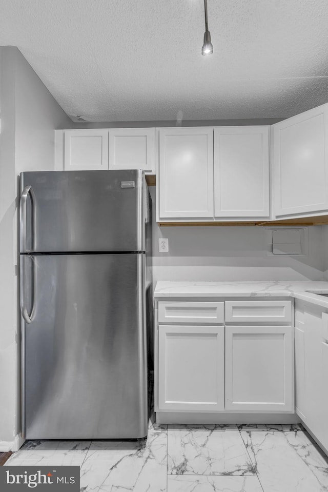 kitchen featuring white cabinetry, stainless steel refrigerator, and a textured ceiling