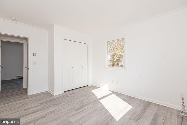 unfurnished bedroom with ornamental molding, a closet, baseboard heating, and light hardwood / wood-style flooring