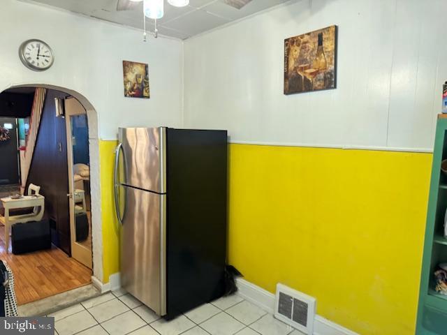 kitchen featuring light tile patterned floors, visible vents, arched walkways, a ceiling fan, and freestanding refrigerator