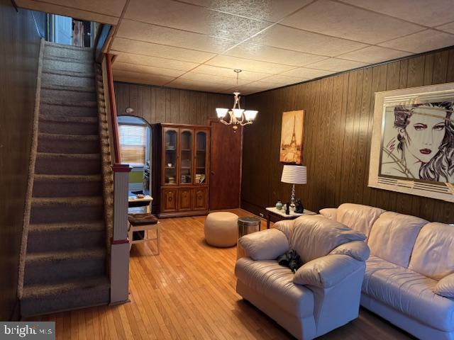 living area featuring wood walls, stairway, wood finished floors, and a notable chandelier