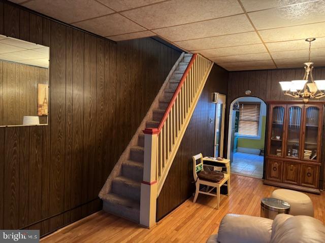 stairs featuring a paneled ceiling, wooden walls, arched walkways, and wood finished floors