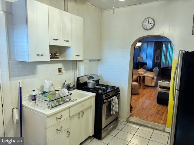 kitchen with light tile patterned floors, arched walkways, white cabinets, appliances with stainless steel finishes, and light countertops