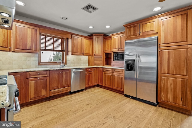 kitchen featuring appliances with stainless steel finishes, sink, decorative backsplash, and light hardwood / wood-style flooring