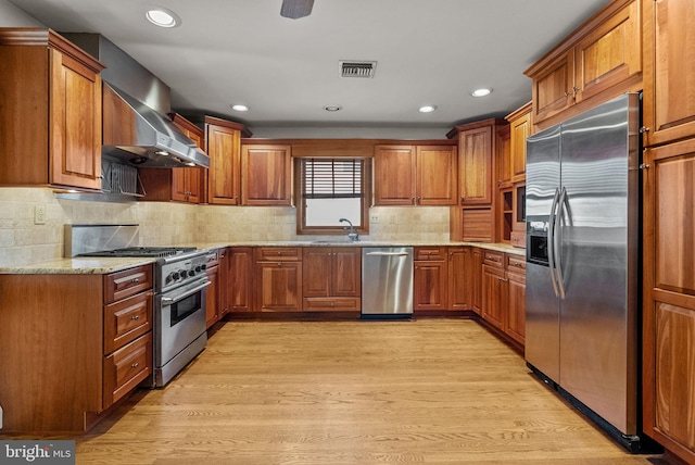 kitchen with sink, stainless steel appliances, light hardwood / wood-style floors, and wall chimney exhaust hood