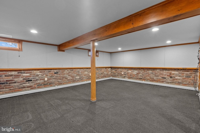 basement featuring ornamental molding, dark colored carpet, and brick wall