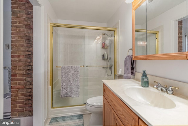 bathroom featuring vanity, a shower with door, toilet, and brick wall