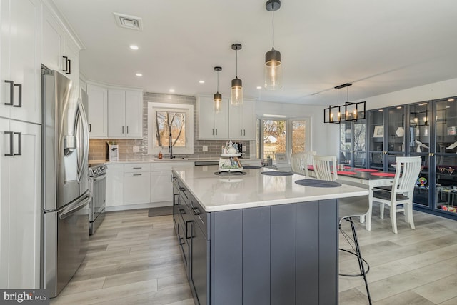 kitchen featuring appliances with stainless steel finishes, hanging light fixtures, a kitchen island, and white cabinets