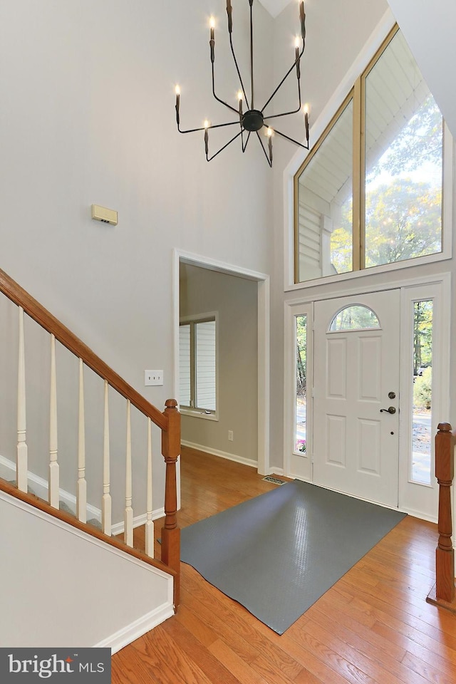 entrance foyer featuring a towering ceiling, wood-type flooring, and a notable chandelier