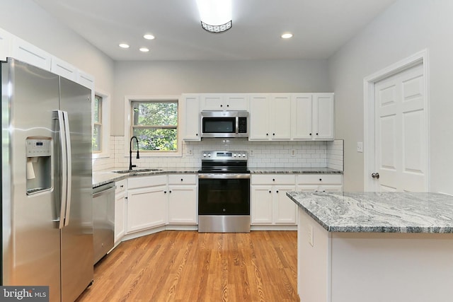 kitchen with sink, white cabinetry, light stone counters, light wood-type flooring, and stainless steel appliances