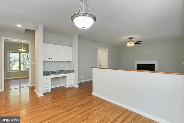 kitchen with white cabinetry, built in desk, hanging light fixtures, light hardwood / wood-style flooring, and ceiling fan