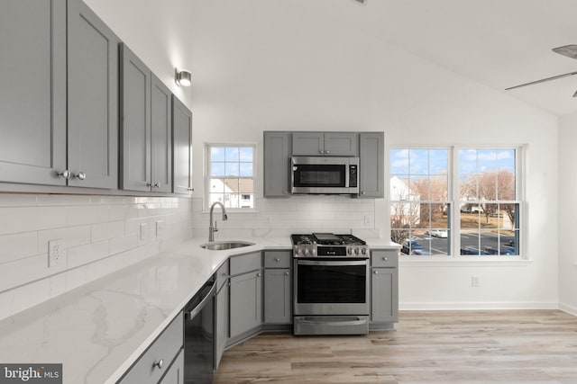 kitchen featuring lofted ceiling, sink, gray cabinetry, stainless steel appliances, and light stone countertops