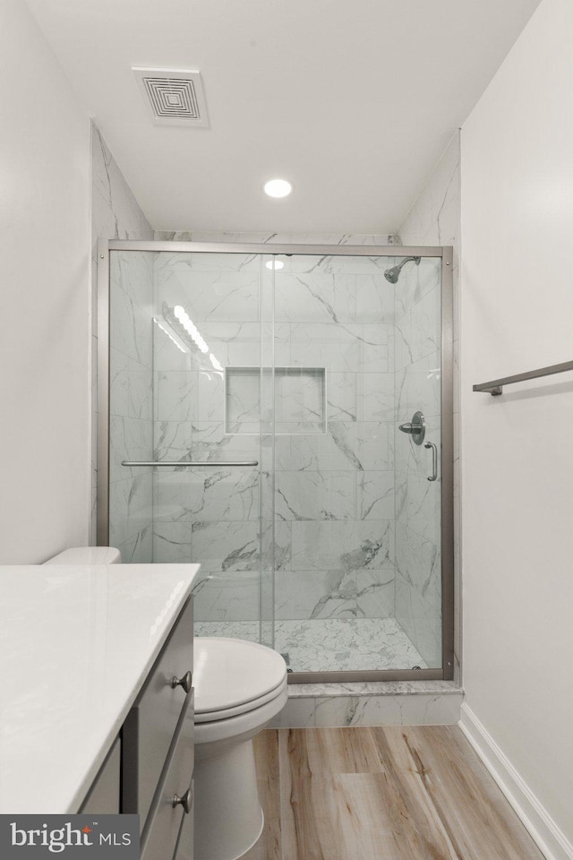 bathroom featuring wood-type flooring, toilet, a shower with shower door, and vanity