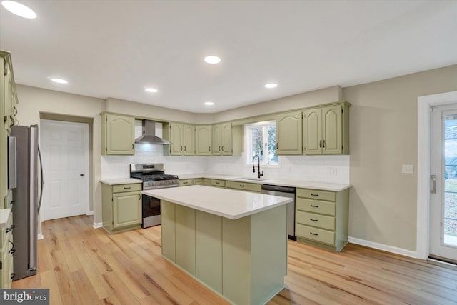 kitchen featuring light hardwood / wood-style flooring, appliances with stainless steel finishes, green cabinetry, a kitchen island, and wall chimney exhaust hood