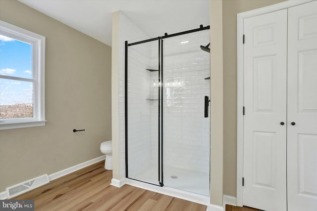 bathroom with wood-type flooring, toilet, and a shower with shower door