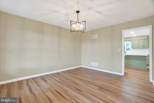 empty room with light hardwood / wood-style flooring and a chandelier