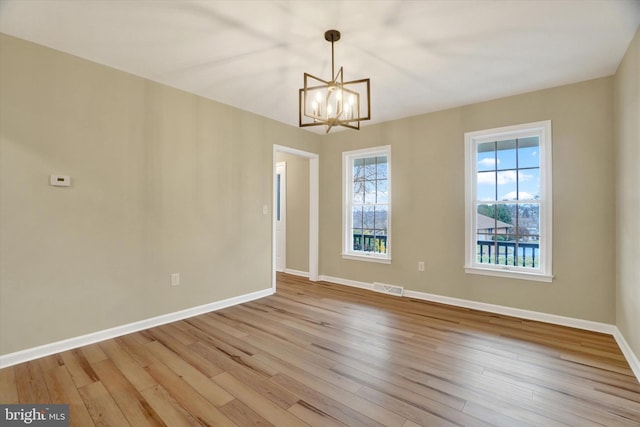 spare room featuring an inviting chandelier and light hardwood / wood-style floors