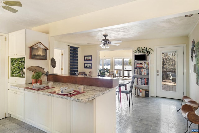 kitchen featuring white cabinets, ceiling fan, kitchen peninsula, light stone countertops, and a textured ceiling