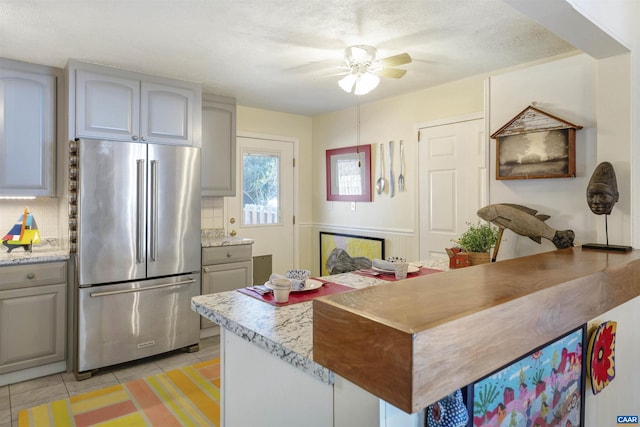 kitchen with gray cabinets, light tile patterned flooring, stainless steel refrigerator, decorative backsplash, and ceiling fan