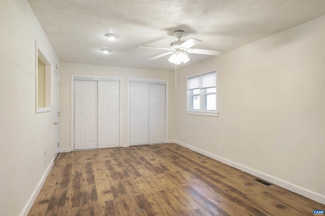 unfurnished bedroom featuring multiple closets, crown molding, dark wood-type flooring, and a textured ceiling