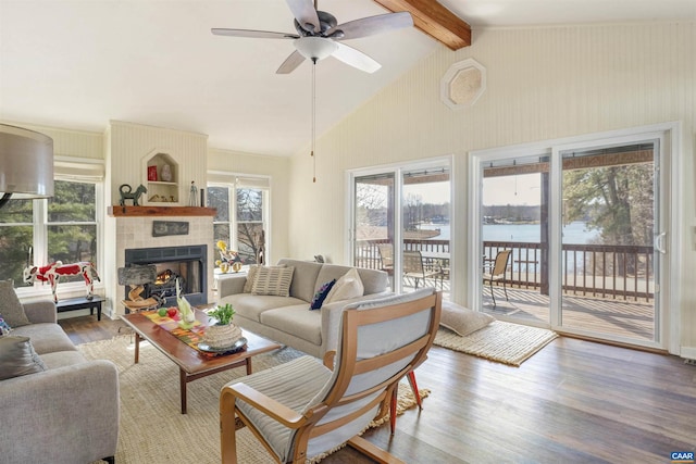 living room with a tile fireplace, hardwood / wood-style floors, ceiling fan, a water view, and beam ceiling