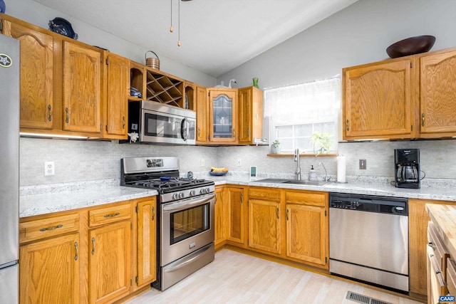 kitchen with sink, appliances with stainless steel finishes, light stone counters, tasteful backsplash, and vaulted ceiling