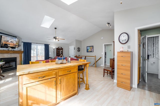 kitchen featuring lofted ceiling with skylight, wooden counters, a tiled fireplace, ceiling fan, and light hardwood / wood-style floors