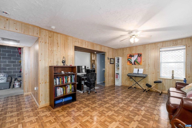 sitting room with ceiling fan, parquet flooring, wooden walls, and a textured ceiling