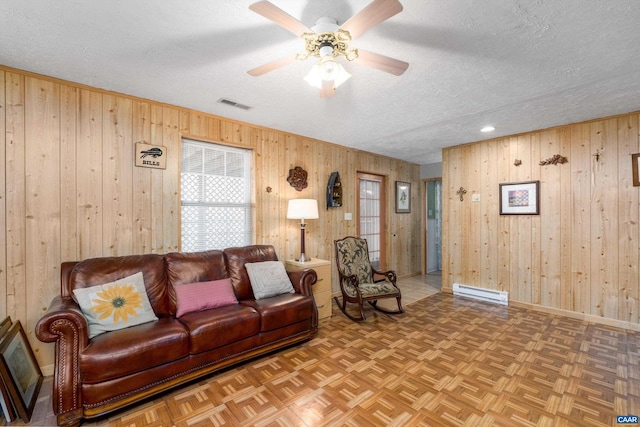 living room featuring ceiling fan, a baseboard heating unit, parquet floors, and a textured ceiling