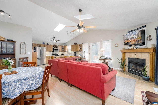 living room with a tiled fireplace, vaulted ceiling with skylight, ceiling fan, and light hardwood / wood-style flooring