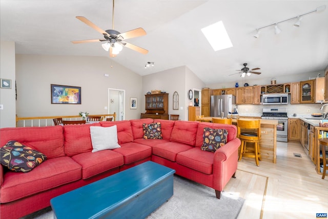 living room with ceiling fan, lofted ceiling with skylight, light hardwood / wood-style floors, and sink