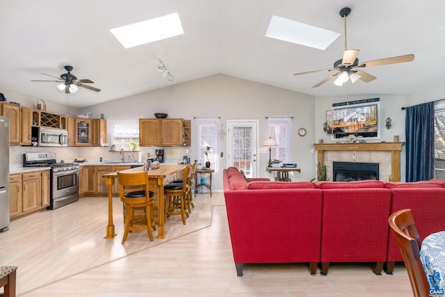 living room with a tile fireplace, lofted ceiling with skylight, ceiling fan, and light hardwood / wood-style floors