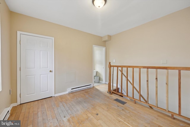 spare room featuring a baseboard heating unit and light wood-type flooring