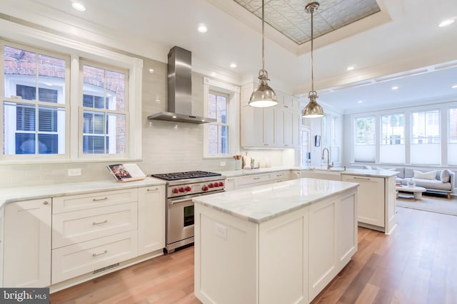 kitchen with white cabinetry, a tray ceiling, high end stainless steel range, decorative light fixtures, and wall chimney exhaust hood