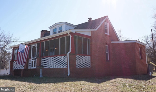 view of property exterior with a lawn, brick siding, a chimney, and a sunroom